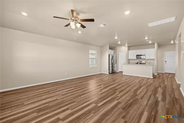a view of an empty room with wooden floor and a kitchen