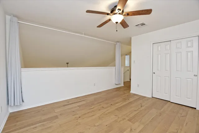 an empty room with wooden floor ceiling fan and windows