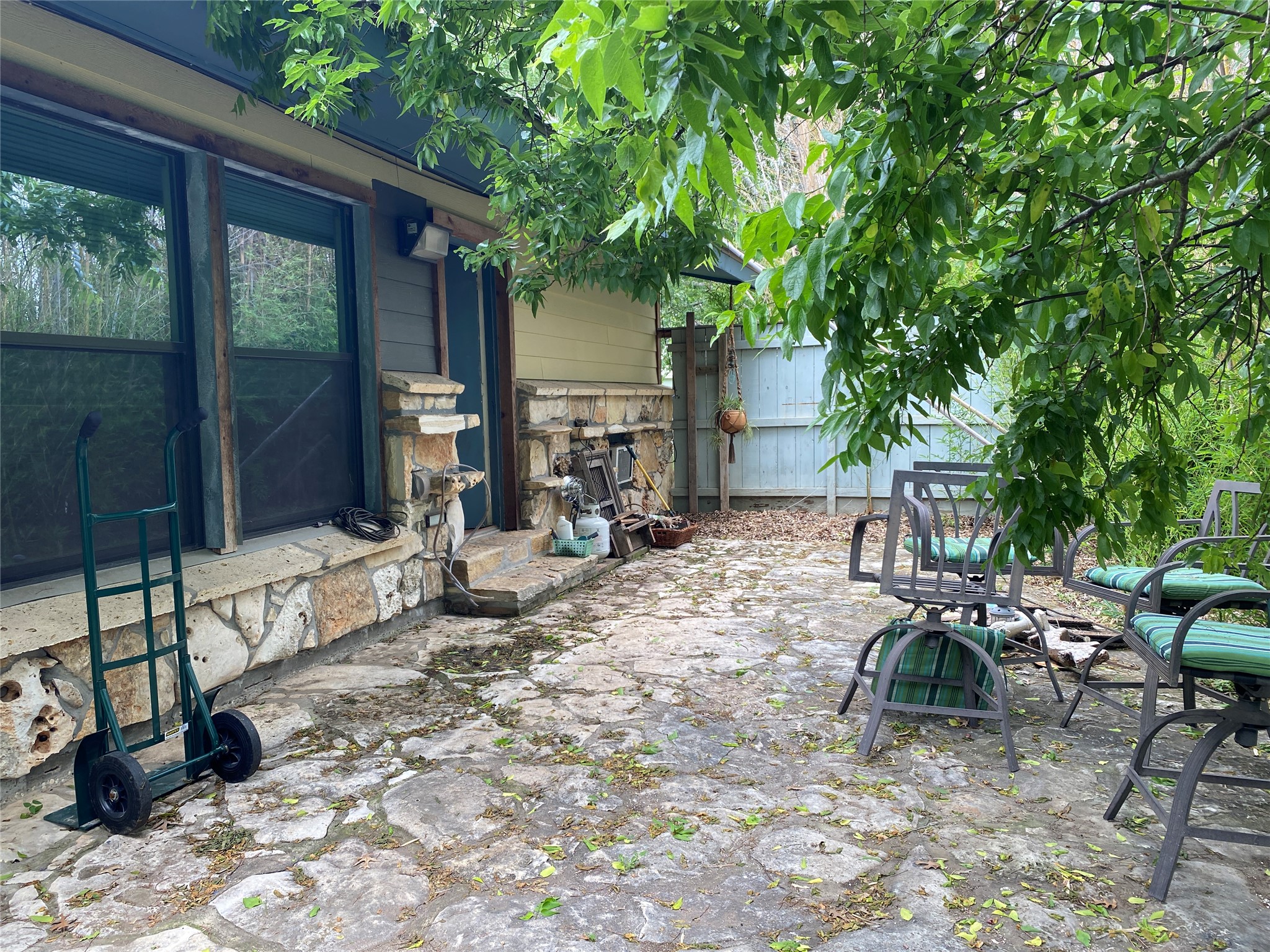 47 Presidio Road Wimberley, TX 78676 - Photo 10 of 12 A flagstone patio extends from a stone-clad exterior, framed by vibrant green foliage.