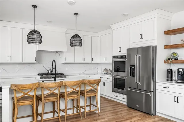 a kitchen with stainless steel appliances granite countertop a refrigerator a sink dishwasher a stove and white cabinets with wooden floor