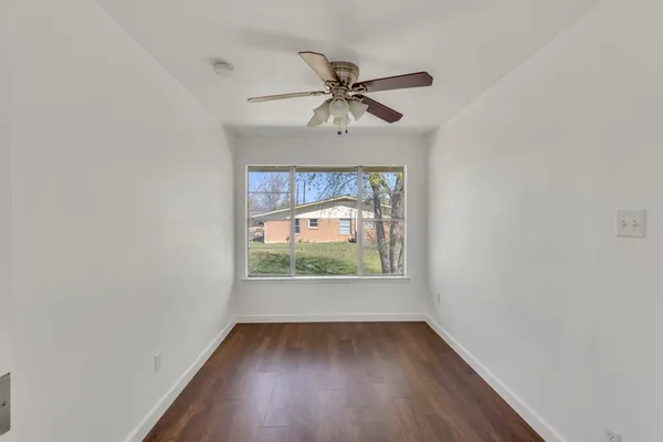 a view of an empty room with window a ceiling fan and wooden floor