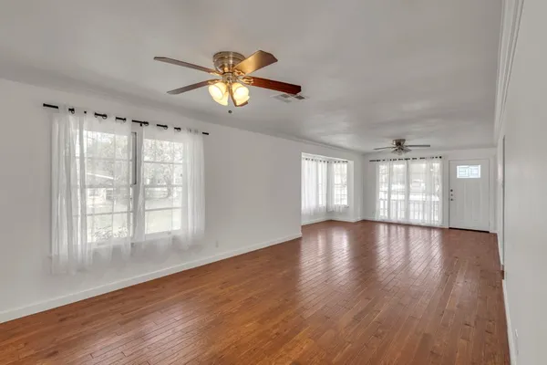 an empty room with wooden floor fan and windows