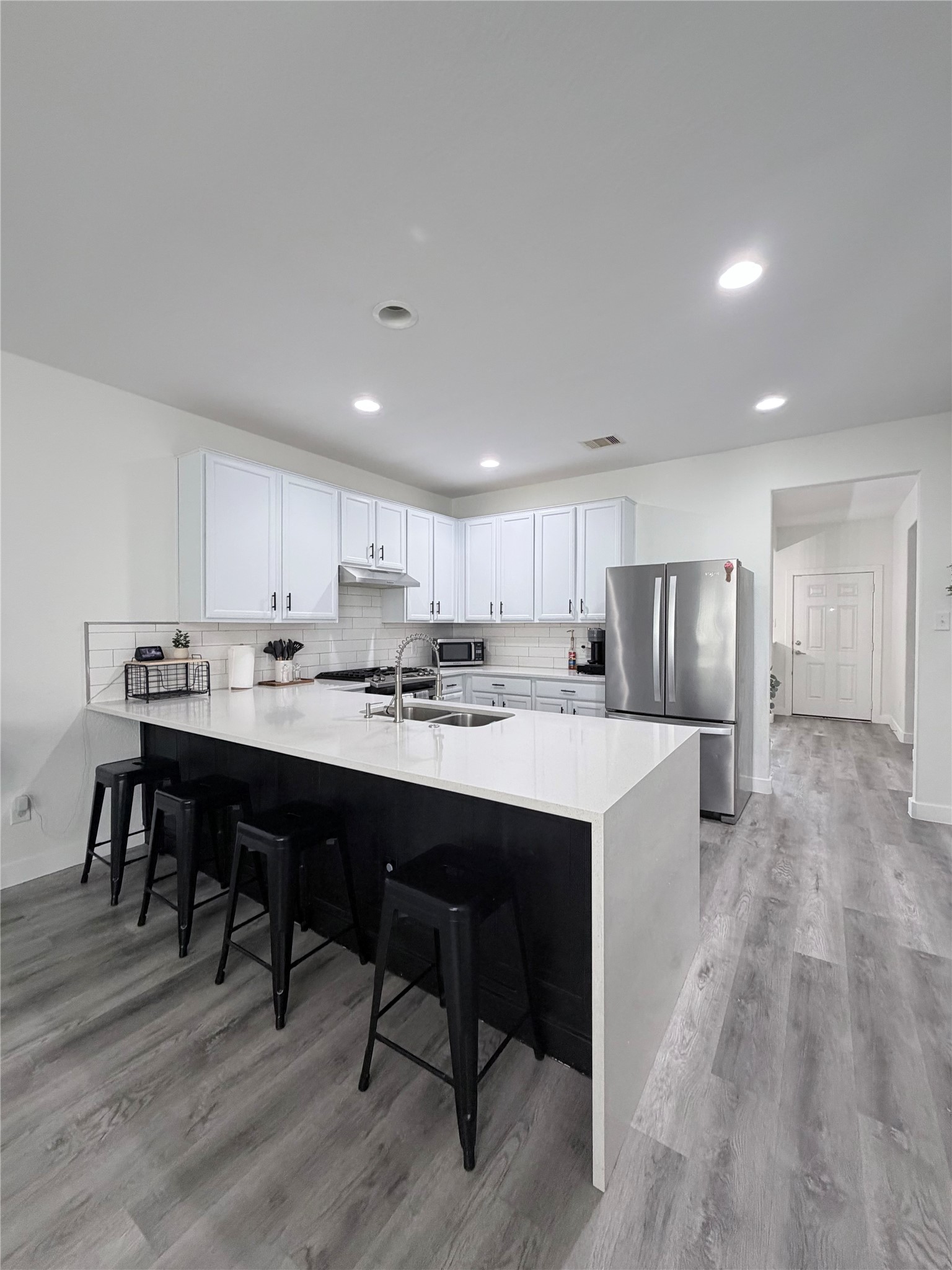 3226 Dappled Vale Trail Spring, TX 77373 - Photo 2 of 26 Modern kitchen with sleek white cabinetry, stainless steel appliances, and a spacious island with bar seating. The open layout features recessed lighting and light wood flooring, creating a bright and inviting space.