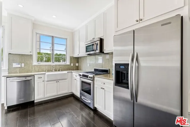 a kitchen with stainless steel appliances granite countertop a refrigerator a stove a sink and white cabinets with wooden floor