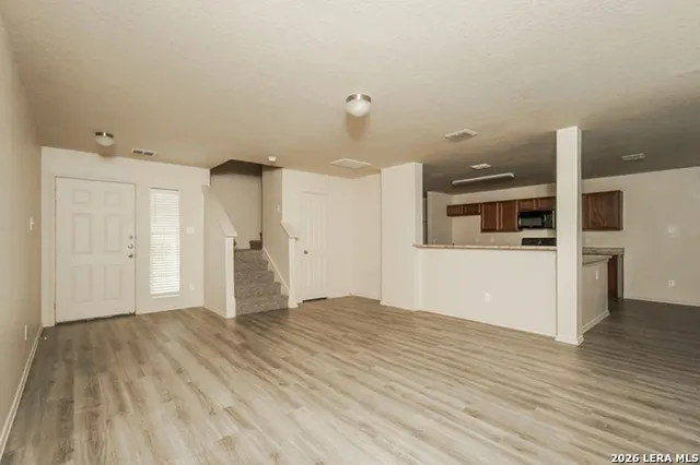 a view of empty room with wooden floor and kitchen