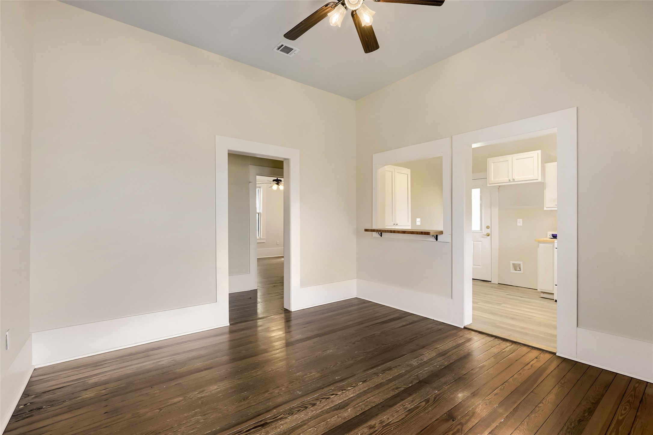 208 North Ave B Elgin, TX 78621 - Photo 7 of 29 This room features elegant hardwood floors, neutral walls, and a ceiling fan with lights. It opens to adjacent rooms with white trim, offering a pass-through to the kitchen, creating a spacious and connected feel.