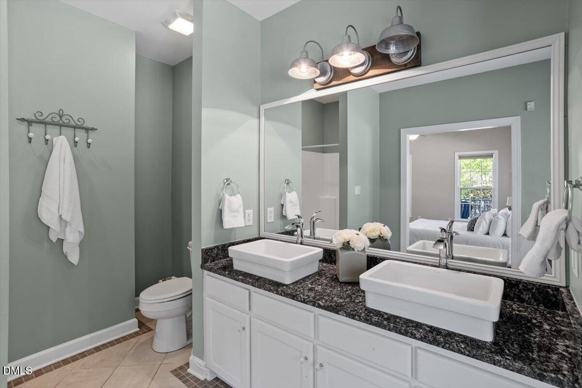 7505 Penny Road Raleigh, NC 27606 - Photo 31 of 35 a bathroom with double vanity sinks a toilet a mirror and shower