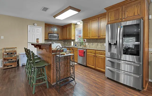 a kitchen with stainless steel appliances granite countertop a refrigerator a stove a sink dishwasher a dining table and chairs with wooden floor