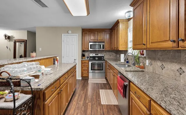 a kitchen with stainless steel appliances granite countertop a sink a stove and a wooden floors