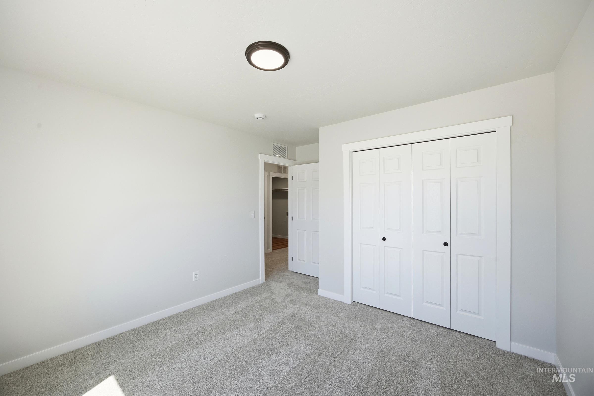 12841 Decatur Street Nampa, ID 83651 - Photo 20 of 30 Spacious room featuring light gray carpeting, neutral wall paint, white bi-fold closet doors with black hardware, white trim, and a flush-mount ceiling light fixture