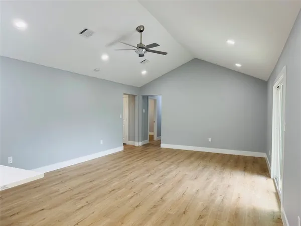 an empty room with wooden floor ceiling fan and windows