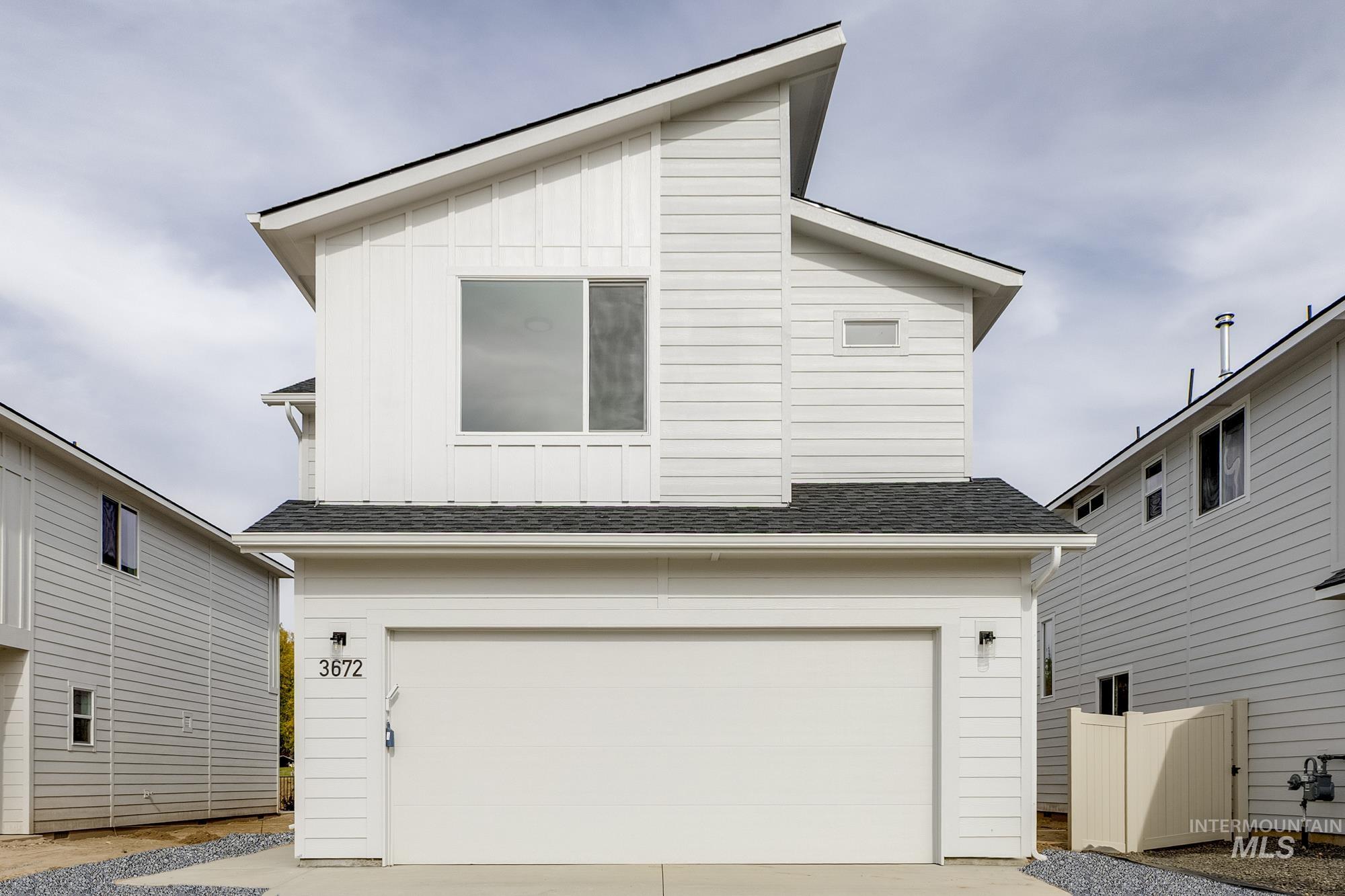 View of front facade with board and batten siding, a shingled roof, a garage, and driveway