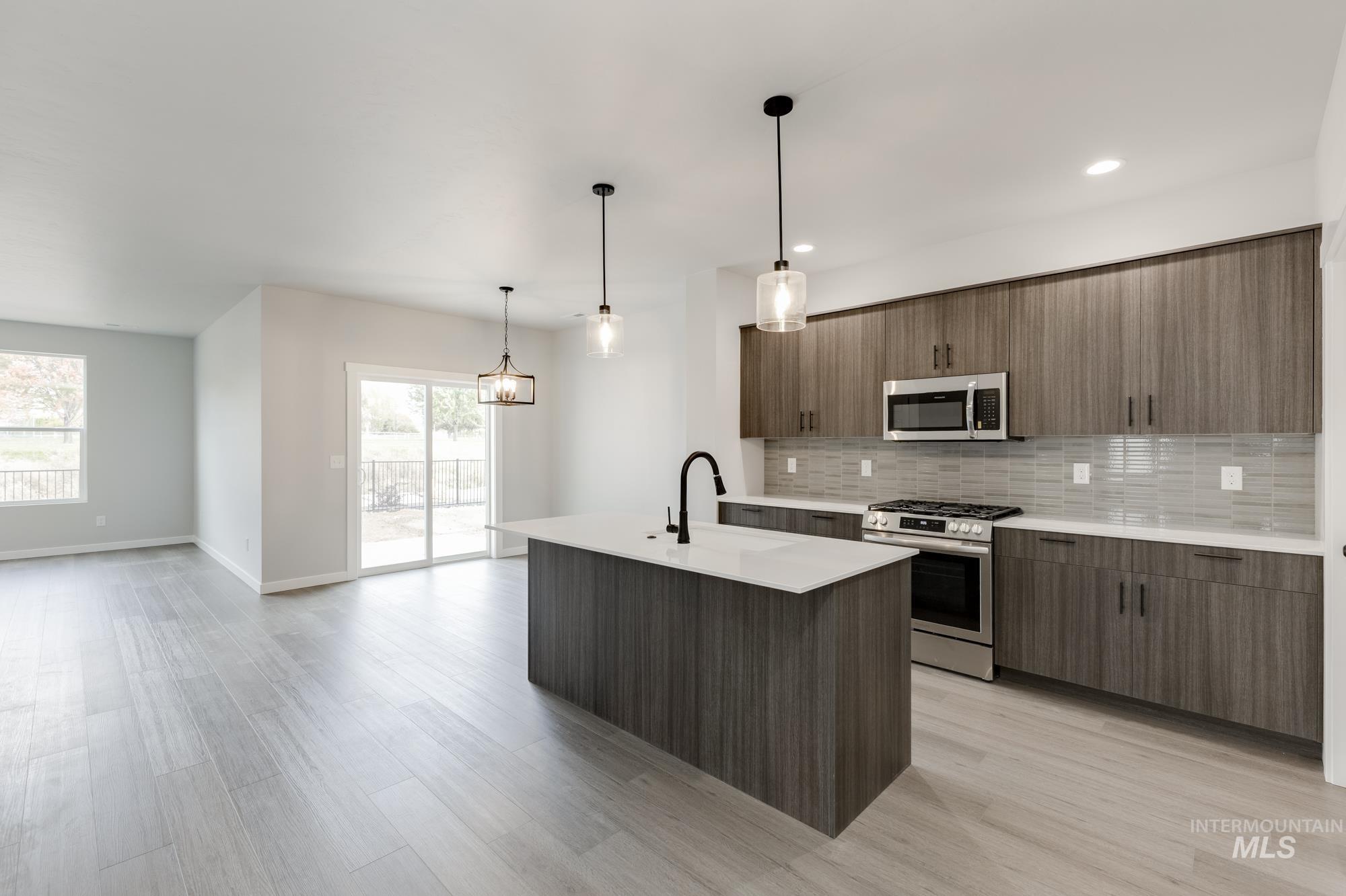 3672 West Dover Drive Meridian, ID 83642 - Photo 3 of 23 Kitchen featuring appliances with stainless steel finishes, backsplash, an island with sink, modern cabinets, and pendant lighting