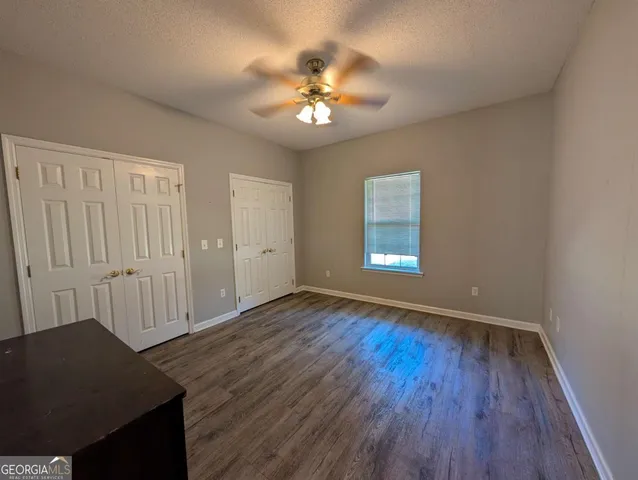 a view of an empty room with wooden floor and a ceiling fan