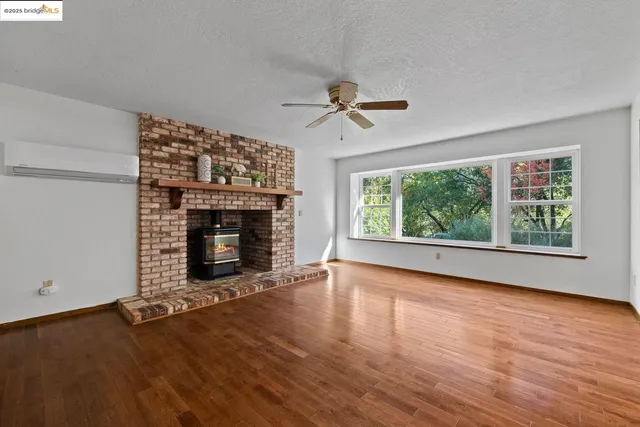 a view of an empty room with wooden floor fireplace and a window