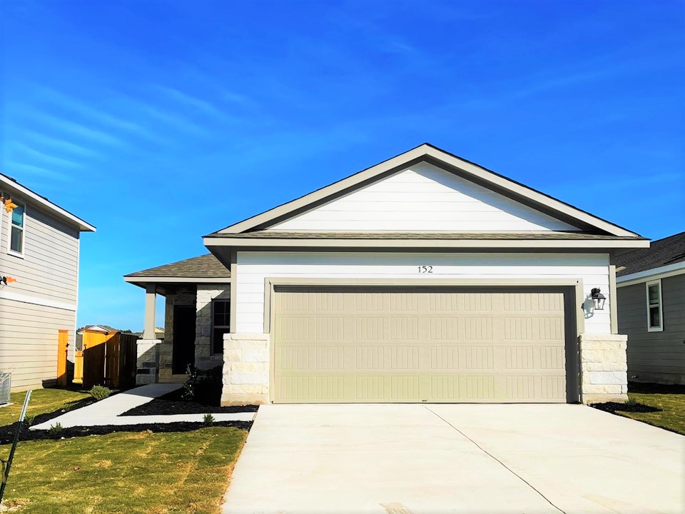 View of front of property featuring a garage, driveway, stone siding, and a front lawn