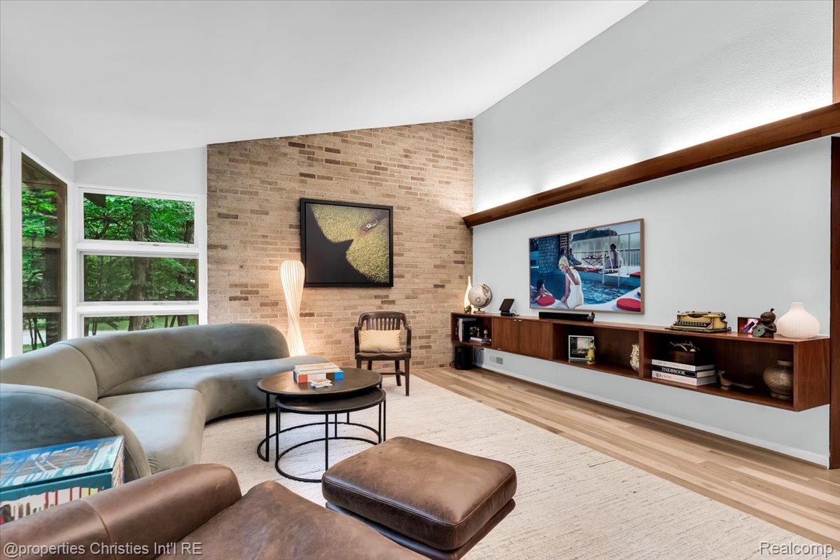 3939 Charing Cross Road Bloomfield Hills, MI 48304 - Photo 10 of 33 Living area featuring a vaulted ceiling with exposed wood beams, a prominent brick accent wall, and a full wall of multi-pane windows