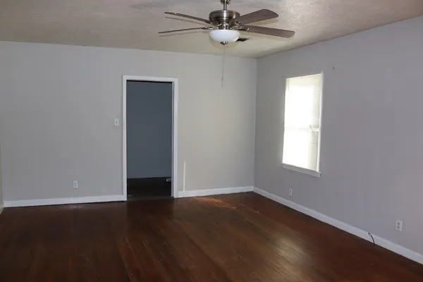 an empty room with wooden floor fan and windows