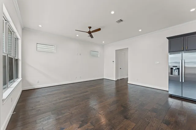 an empty room with wooden floor ceiling fan and windows