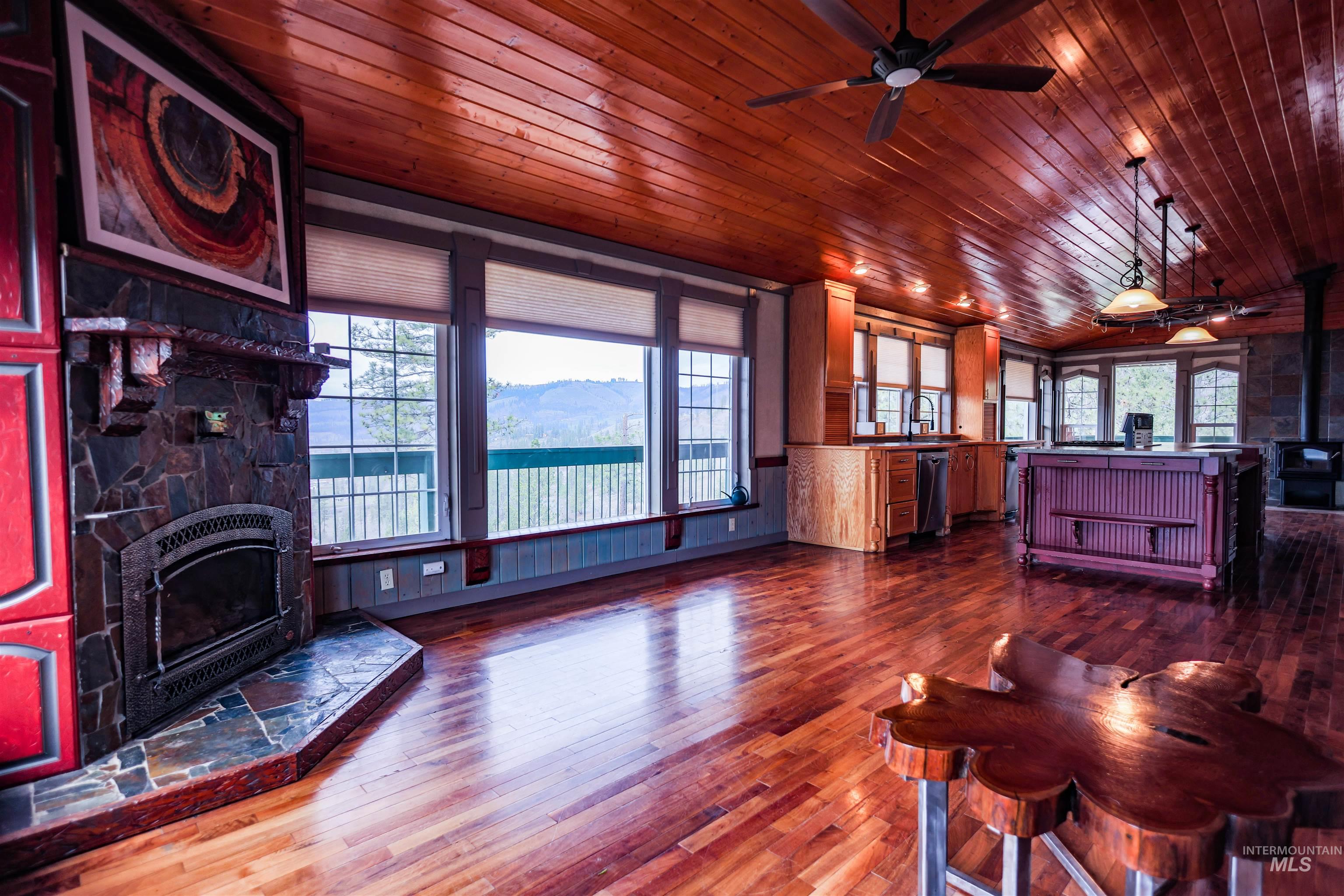 402 Beaverslide Road Kamiah, ID 83536 - Photo 15 of 46 Living area with a ceiling fan, dark wood-style floors, a wood stove, a stone fireplace, and wooden ceiling