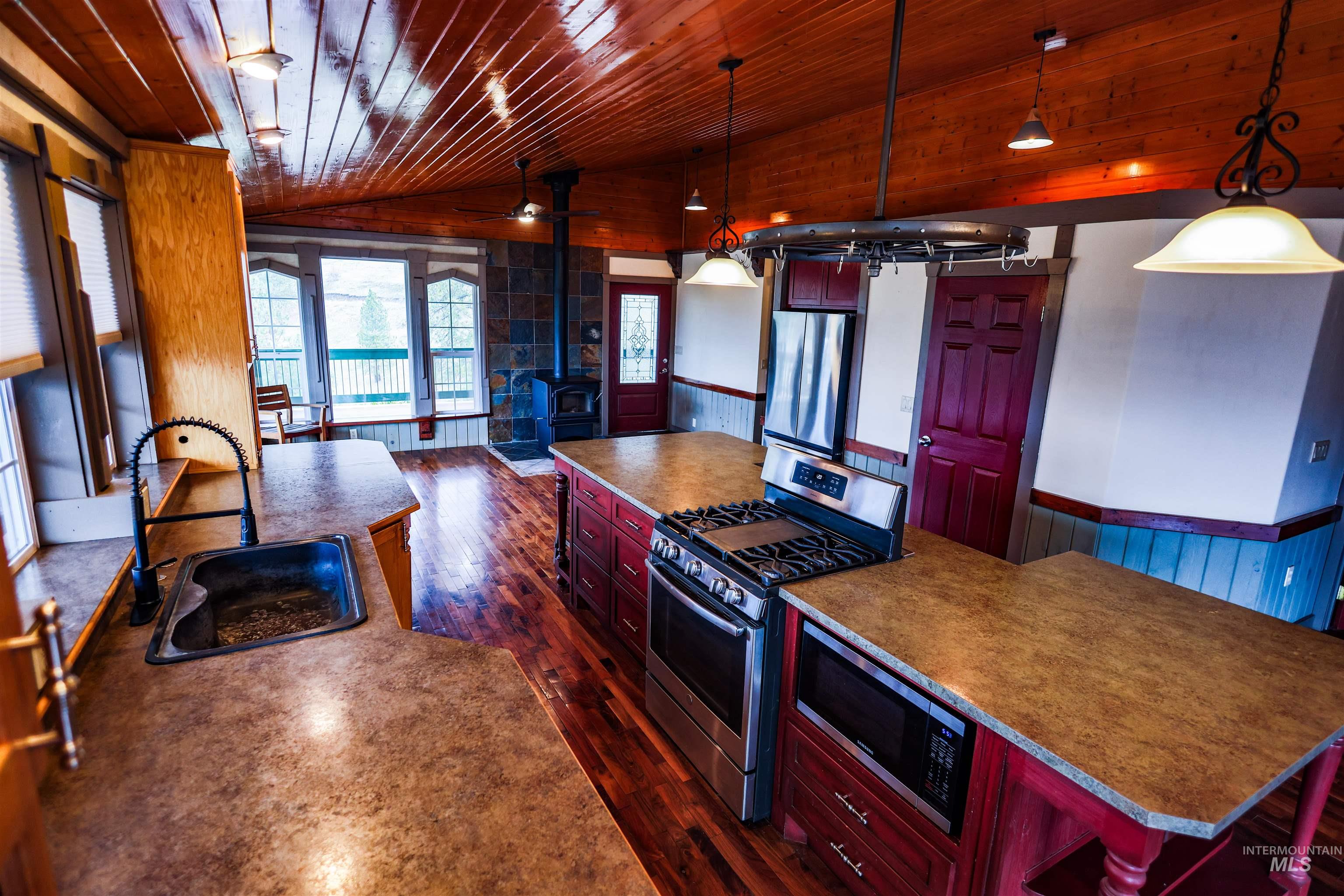402 Beaverslide Road Kamiah, ID 83536 - Photo 18 of 46 Kitchen featuring a wainscoted wall, a wood stove, wooden walls, reddish brown cabinets, and stainless steel appliances