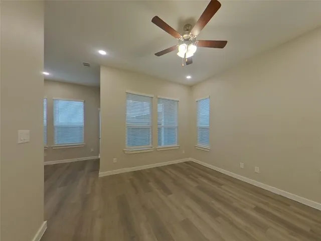 an empty room with wooden floor fan and windows
