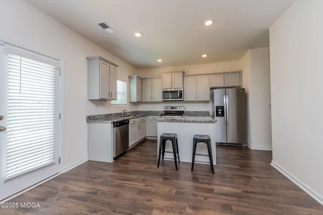 a kitchen with stainless steel appliances granite countertop a refrigerator a stove top oven and white cabinets