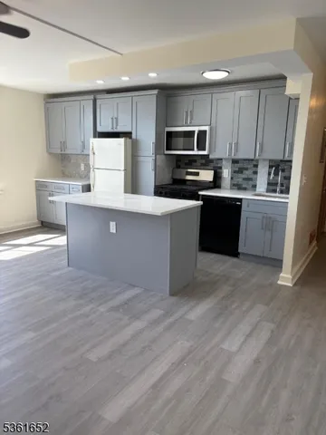 a kitchen with kitchen island granite countertop a stove top oven a refrigerator a sink and dishwasher with wooden floor