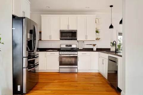 a kitchen with granite countertop a refrigerator oven a sink and white cabinets