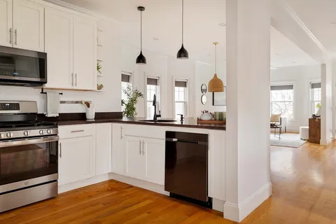 a kitchen with stainless steel appliances granite countertop a stove a sink and white cabinets with wooden floors