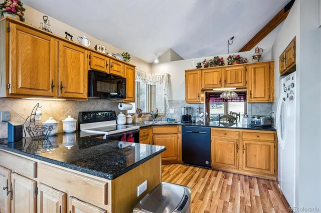 a kitchen with stainless steel appliances granite countertop a stove top oven a sink dishwasher a dining table and chairs with wooden floor