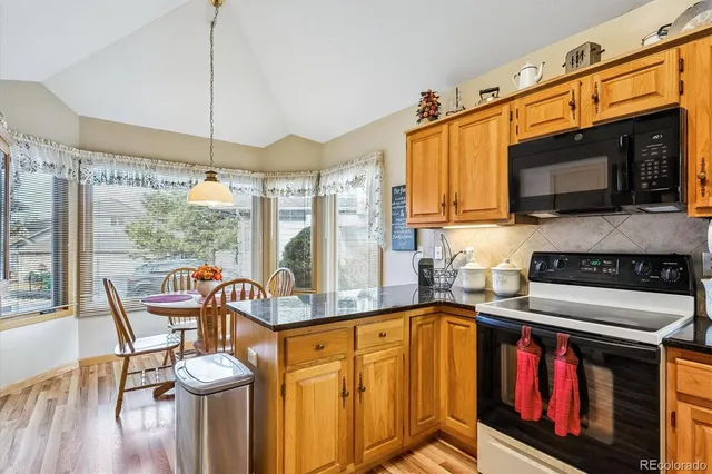 a kitchen with stainless steel appliances granite countertop a stove top oven a sink a dining table and chairs with wooden floor