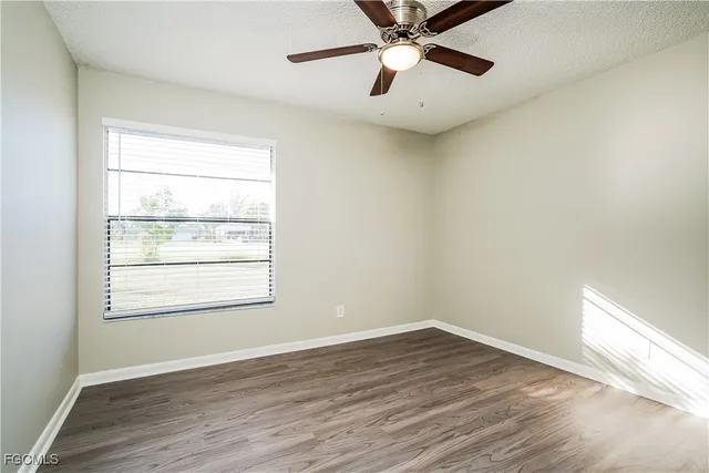 an empty room with wooden floor fan and windows