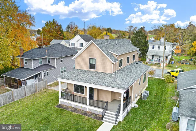 a view of a white house with a large windows and a yard with plants and large trees