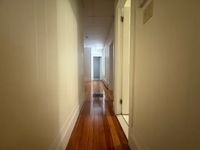 a view of a hallway with wooden floor and a bathroom