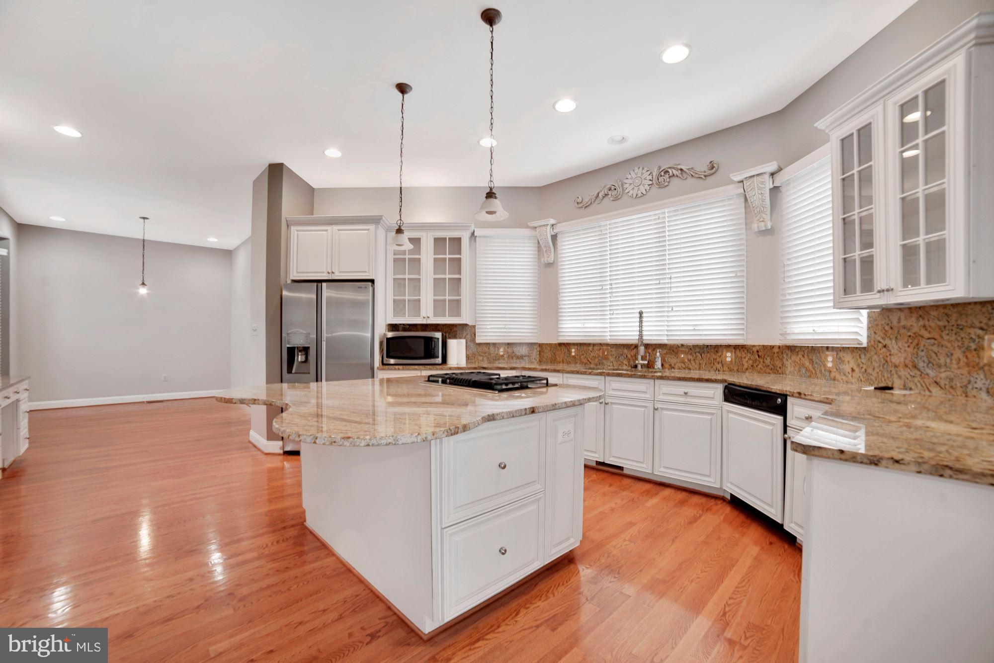 8238 Snead Loop Gainesville, VA 20155 - Photo 3 of 49 a large white kitchen with stainless steel appliances granite countertop a stove a sink a refrigerator and white cabinets with wooden floor