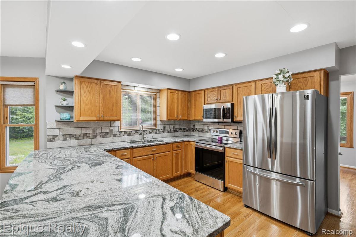 1221 Rhodes Road Lake Orion, MI 48360 - Photo 18 of 72 Kitchen featuring an expansive island with a patterned countertop, wood cabinetry, stainless steel appliances, a tiled backsplash, and recessed lighting