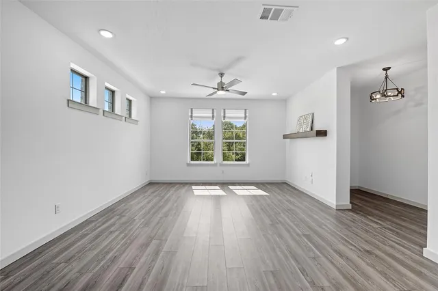 an empty room with wooden floor chandelier and windows