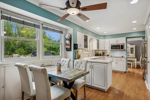 a open dining room with stainless steel appliances granite countertop hardwood floor a ceiling fan furniture a large window and a kitchen view