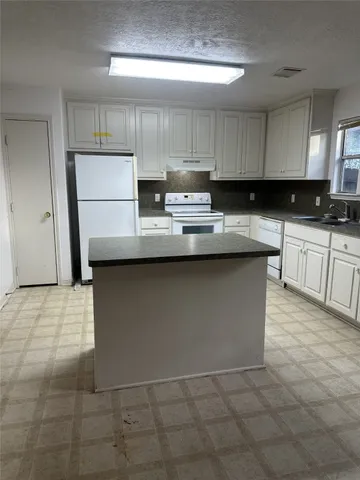 a kitchen with kitchen island granite countertop a sink a stove a refrigerator and cabinets