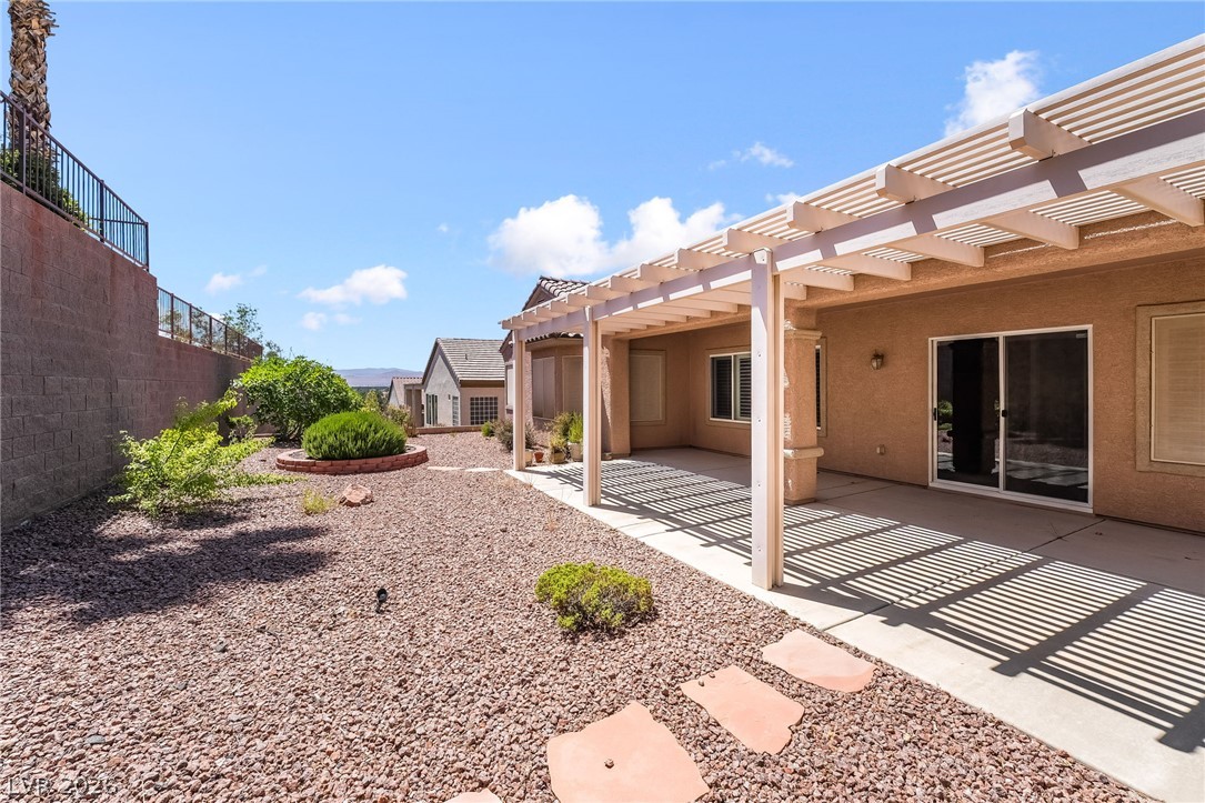 3033 Hartsville Road Henderson, NV 89052 - Photo 38 of 41 A spacious backyard with a concrete patio, shaded by a wooden pergola, features desert-friendly landscaping.