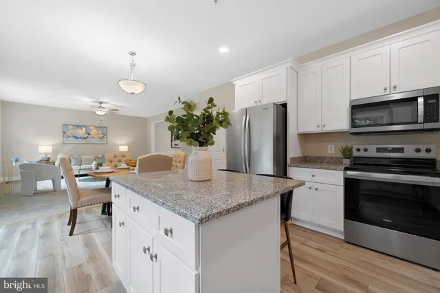 a kitchen with stainless steel appliances granite countertop a sink dishwasher a microwave oven a refrigerator with white cabinets and wooden floor
