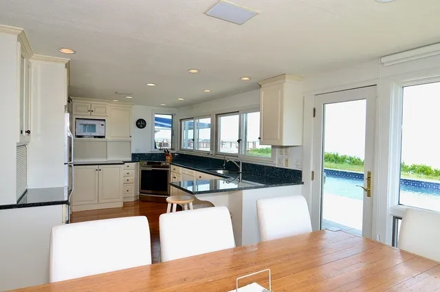 a living room with stainless steel appliances kitchen island granite countertop a table chairs and a living room view