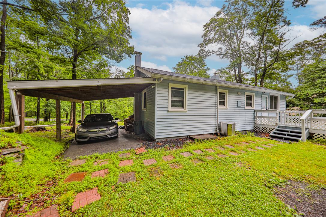 5599 Minks Pond Road Bushkill, PA 18324 - Photo 48 of 64 A welcoming carport shields your vehicle, nestled beside a charming home with a practical deck and surrounding greenery.