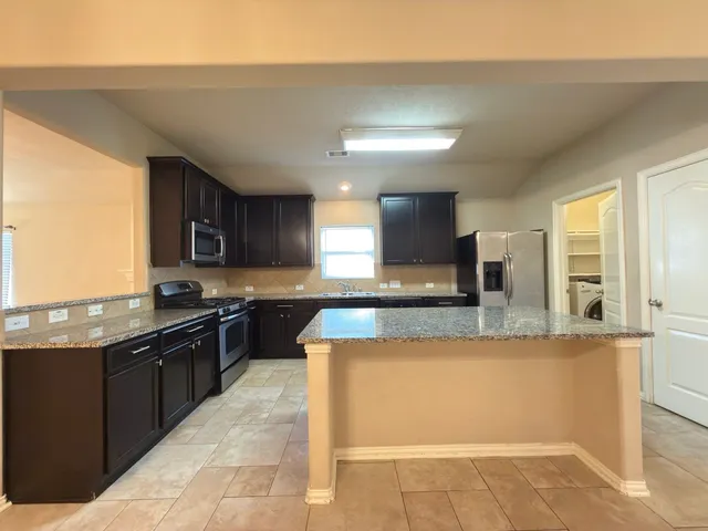 a large kitchen with a large counter top space a sink and stainless steel appliances
