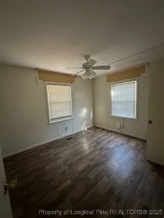 an empty room with wooden floor windows and fan