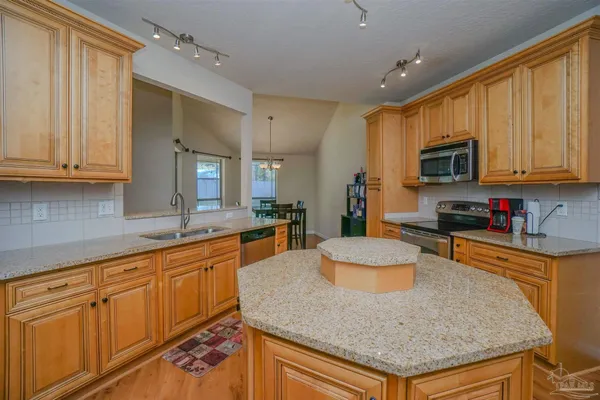 a kitchen with granite countertop a stove a sink a dining table and chairs with wooden floor