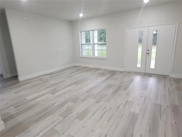 an empty room with wooden floor and kitchen view