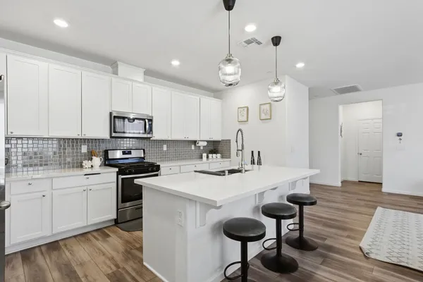 a kitchen with a sink a stove a refrigerator and white cabinets with wooden floor
