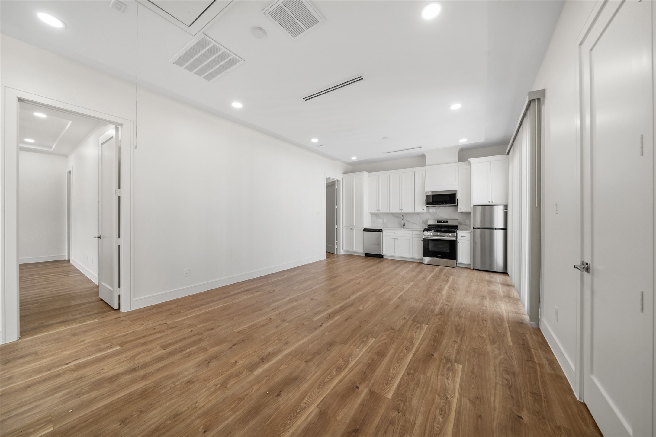 1839 Colquitt Street Houston, TX 77098 - Photo 16 of 19 Modern, open-concept kitchen and living area with wood floors and recessed lighting. The kitchen features white cabinetry, stainless steel appliances, and a sleek design. The space is bright and inviting, perfect for entertaining or relaxed living.